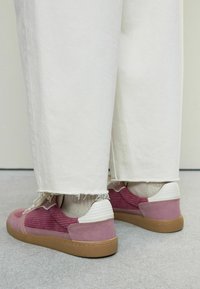 Rosa och vita sneakers med ribbad textur, en brun gummisula och beige snören, parat med fransiga vita jeans.