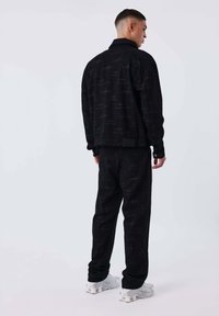 Giacca e pantaloni in corduroy neri con un sottile motivo, caratterizzati da un colletto e una vestibilità rilassata. Modello che indossa sneaker bianche.