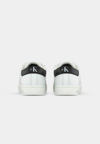 White sneakers with a smooth leather finish, featuring a black synthetic heel panel and logo accent. Low-top design; textured rubber sole.