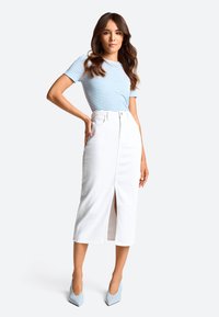 Gonna midi in denim bianco con uno spacchetto frontale, abbinata a una maglietta corta a righe blu. Il modello indossa tacchi a punta azzurri.