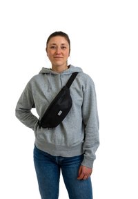 Čierny látkový pásový vak nosený cez telo, so zipsom a značkovou nášivkou. Šedá mikina a modré džínsy dopĺňajú outfit.