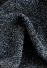 Tamno siva vuna s materijal s mekanom, pahuljastom teksturom i vidljivim vlaknima, prikazana u slobodnim, zakrivljenim naborima.