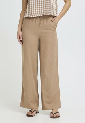 Donna che indossa pantaloni beige a gamba larga con vita elasticizzata e coulisse, abbinati a sandali infradito neri e top a quadri.