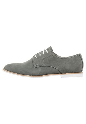 Chaussure de soirée en daim gris avec des lacets blancs, bout rond et profil élancé. Présente une semelle contrastante claire. Design épuré et minimal.