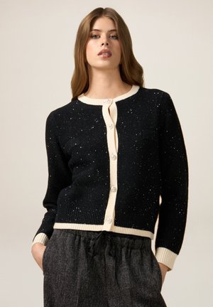 Cardigan nero con rifiniture crema, caratterizzato da un collo rotondo e bottoni perle. Il tessuto ha una texture maculata con un effetto luccicante.