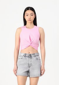 Roosa ilma varrukat crop top, millel on keerdunud esidetail, koos heledate hallide denimpükstega, millel on keeratud äärte ja ees taskud.
