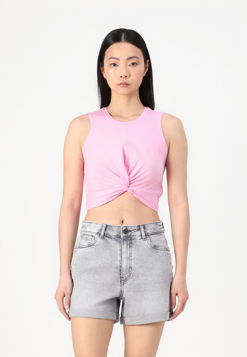 Roosa ilma varrukat crop top, millel on keerdunud esidetail, koos heledate hallide denimpükstega, millel on keeratud äärte ja ees taskud.