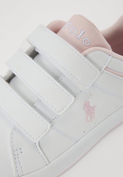 Fehér sneaker rózsaszín kiegészítőkkel, tépőzáras pántokkal és texturált rózsaszín sarkával. Oldalán egy apró rózsaszín hímzett logóval rendelkezik.