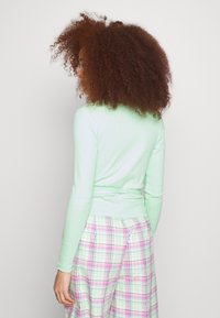 Długi rękaw miętowy top o dopasowanym kroju i marszczonym pasie, w połączeniu z szerokimi spodniami w pastelową kratkę w kolorze różowym, zielonym i czarnym.