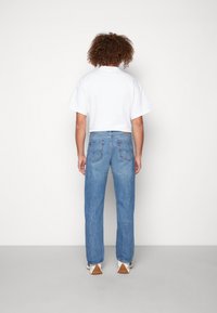 White short-sleeve t-shirt paired with light blue straight-leg jeans. Denim features two back pockets and a classic design with minimal detailing.