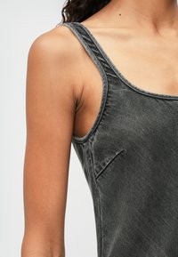 Top de tirantes de denim gris con escote redondeado, tirantes delgados y textura sutil. Presenta un bolsillo en ángulo en el lado izquierdo.