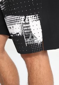 Schwarze Sportshorts mit weißen grafischen Mustern aus Punkten und Streifen. Enthält ein Reebok-Logo an der unteren Seite. Hergestellt aus leichtem Material.