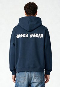 Navyblauwe hoodie met een voorste kangoeroezak, voorzien van witte "MIRA PARIS" tekst op de achterkant. Zachte stof en geribbelde manchetten.