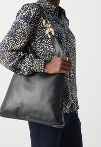Borsa a mano in pelle nera con una texture liscia, dettagli in hardware dorato e un design semplice e senza fronzoli. Tracolla per un facile trasporto.