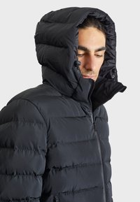 Black puffy jacket with a high collar and adjustable hood, featuring vertical seams, front zipper, and a smooth, shiny fabric texture.