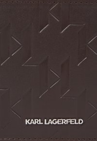 Pruun nahkne rahakott, millel on reljeefne geomeetriline muster, ja alumisel serval hõbedane logo "KARL LAGERFELD". Sile tekstuur ja puhtad jooned.