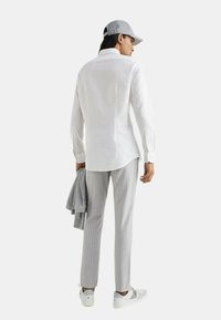 Camicia bianca in lino a maniche lunghe abbinata a pantaloni grigi a righe sottili e un berretto grigio chiaro. Un maglione grigio è appoggiato su un braccio.