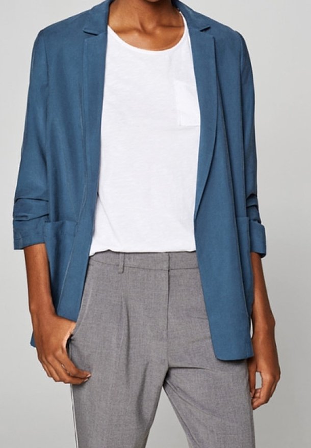Blauer Blazer aus leichtem Stoff mit lockerem Schnitt, versehen mit hochgekrempelten Ärmeln, offenem Vorderteil und Seitentaschen, getragen über einem weißen Hemd.