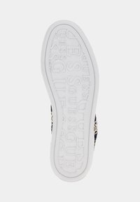 Biała podeszwa buta z wypukłym wzorem logo "GUESS" powtarzającym się na całej powierzchni, prezentująca teksturowany design zapewniający przyczepność.