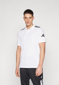 T-shirt polo blanc avec un col et trois rayures noires sur les épaules. Le tissu semble lisse et léger. Marquage noir sur le bras.