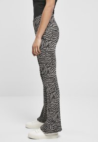 Pantaloni a zampa d'elefante grigi con motivo a strisce zebra nere. Realizzati in un materiale morbido, presentano una vita alta e sono abbinati a sneaker bianche.