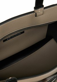 Interno di una borsa a tracolla sintetica beige con accenti neri, scomparto con zip e etichetta Armani Exchange; texture liscia e forma strutturata.