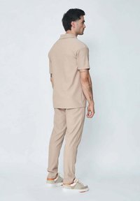 Polo beige et pantalon assorti en tissu lisse. La tenue présente un col classique et une coupe décontractée, associée à des baskets multicolores.