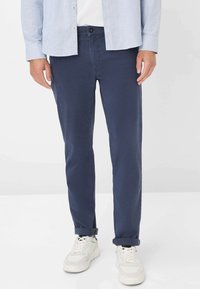 Marineblaue Baumwollchinos mit schlanker Passform, ausgestattet mit Vordertaschen und hochgeschlagenen Säumen, kombiniert mit weißen Sneakers.