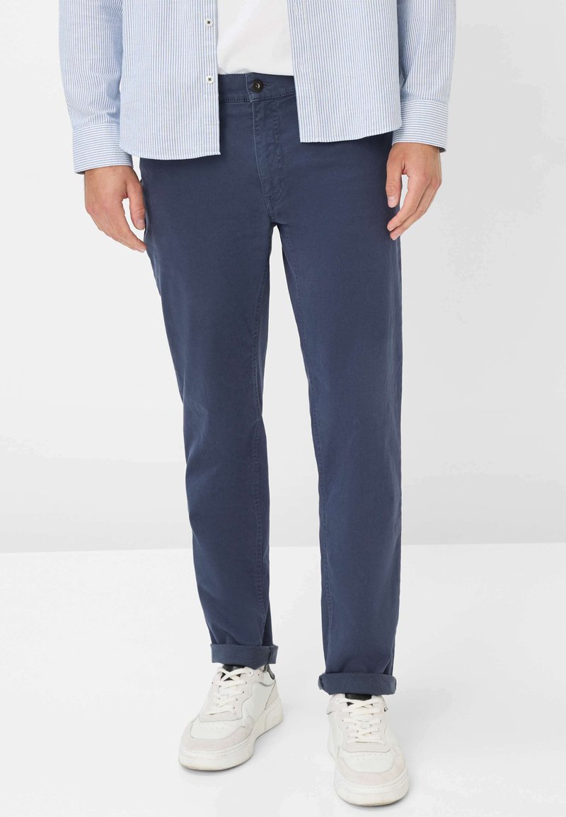Marineblaue Baumwollchinos mit schlanker Passform, ausgestattet mit Vordertaschen und hochgeschlagenen Säumen, kombiniert mit weißen Sneakers.