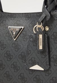 Czarna syntetyczna torba na ramię z wytłoczonym wzorem logo, z trójkątnym metalowym logo, złotymi akcentami i odpinanym znakiem.