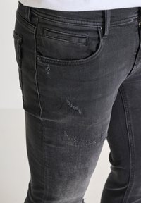 Crne traperice s slim fit krojem, koje sadrže istrošene detalje i blago izblijeđeni izgled, istaknute stražnjim džepom s etiketom.
