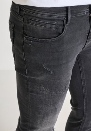 Zwarte denim jeans met een slim fit, voorzien van versleten details en subtiele vervaging, benadrukt door een achterzak met een label.