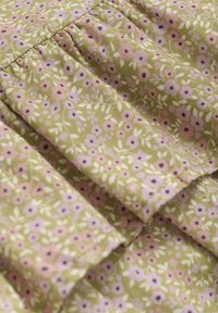 Grön tyg med ett blommönster som har rosa och lila blommor och gröna blad. Texturen är mjuk med veckade detaljer.