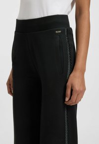 Zwarte wijde broek met een textuurstof. Kenmerkt zich door een geribde tailleband, zijzakken en een contrasterend gevlochten ontwerp langs de naden.