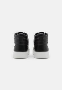 Zapatillas altas de cuero negro con una textura suave, suela de goma blanca y detalles de costura sutil en la parte trasera.