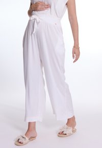 Witte, lichte stof broek met een relaxte pasvorm. Voorzien van een elastische tailleband met een strik en een verkorte lengte. Gemaakt om te dragen met tan, fluffy slides.
