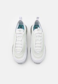 Bílé tenisky s aerodynamick ým designem, se zelenými akcenty, texturovanými materiály a charakteristickou vzorovanou stélkou. Viditelná gumová podrážka.