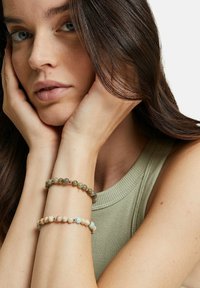 Två pärlarmband bärs på ett handled, det ena med grå-gröna stenar och metalliska detaljer, det andra med ljusare, fläckiga stenar.