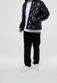 Svart uppblåsbar jacka med glansig yta, vit t-shirt under, svarta kordbyxor och vita sneakers. Har ribbat krage och dragkedjestängning.