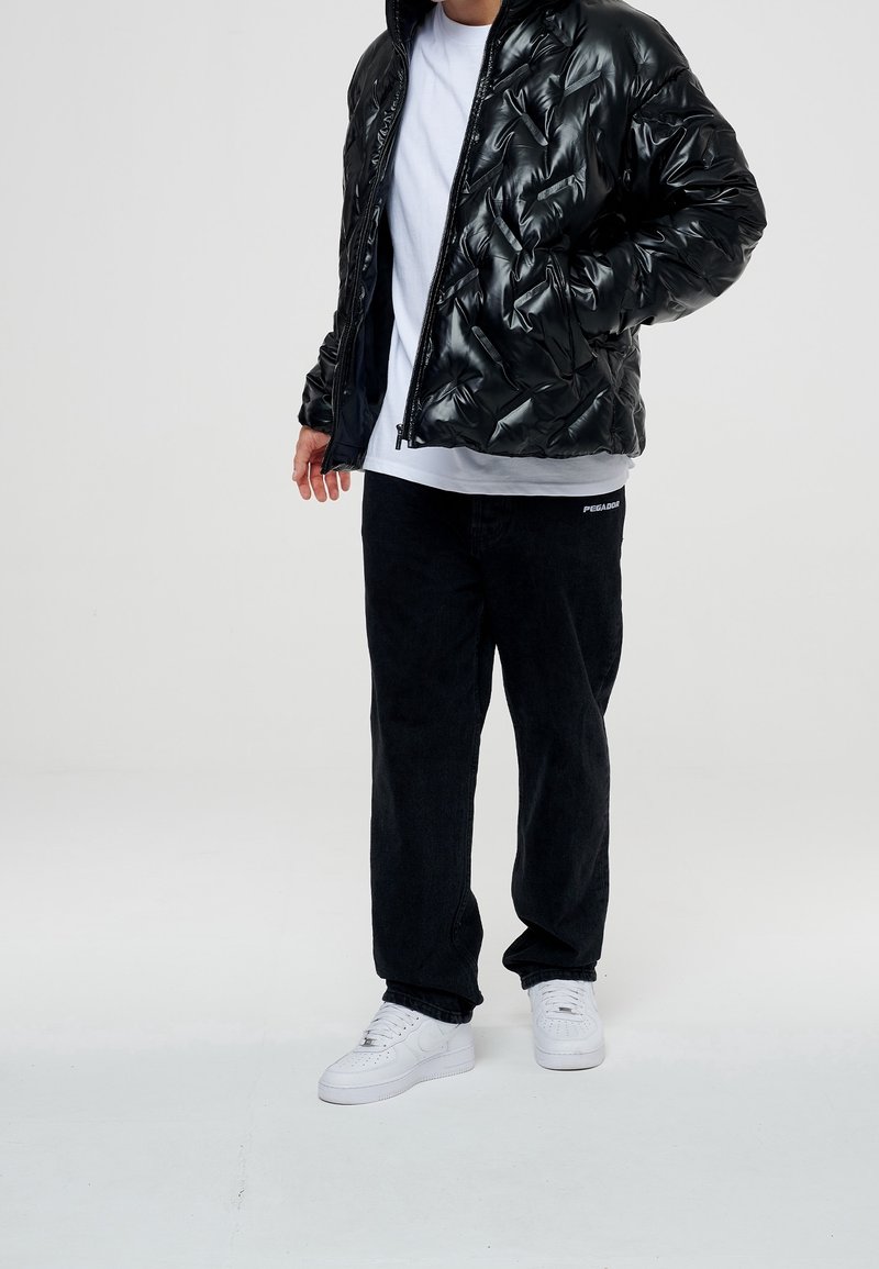 Svart uppblåsbar jacka med glansig yta, vit t-shirt under, svarta kordbyxor och vita sneakers. Har ribbat krage och dragkedjestängning.