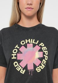 Black cotton T-shirt featuring a large, multi-colored band logo design with pink and yellow text stating "RED HOT CHILI PEPPERS."
