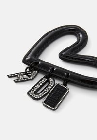 Svart hjerteformet håndtak laget av glanset materiale, med tre merkelapper: en med rhinestones, en med teksten "D" og en annen med "DIESEL."