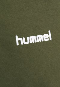 Tessuto verde oliva con una texture a righe che presenta un prominente logo bianco "hummel". Il design è semplice e moderno.