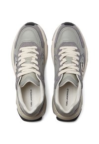 Pelēkas kedas ar ādas un zamšāda materiāliem, noapaļota forma, biezas baltas auklas un melna akcenta detaļa uz papēža. Logo izdrukāts iekiekšē.