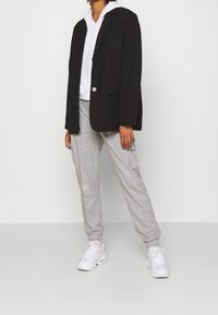 Svart blazer med en enda knapp, kombinerad med en vit hoodie och gråa sweatpants. Beige accenter på skorna. Avslappnad lagerpåläggningsoutfit.