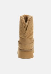 Stivale alla caviglia in suede beige con punta arrotondata, fodera in pelliccia calda, cuciture decorative e tacco in gomma basso. Caratterizzato da un dettaglio fibbia laterale.
