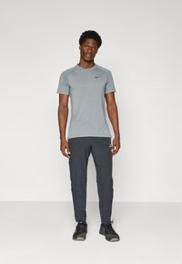 Szürke, rövid ujjú Nike póló sötétszürke Nike nadrággal párosítva. Könnyű anyag, sportos fazon, fekete logóval a mellkason.