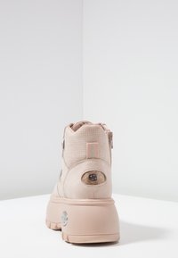 Ljusrosa ankelskor med en texturerad mockaövre, dragkedjestängning och en kraftig plattformssula. Har en cirkulär logotypdekoration på klacken.