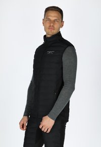 Schwarze Steppweste mit hohem Kragen, Reißverschluss vorne und Taschen. Sie hat eine gesteppten Textur und ein Logo auf der oberen linken Seite.