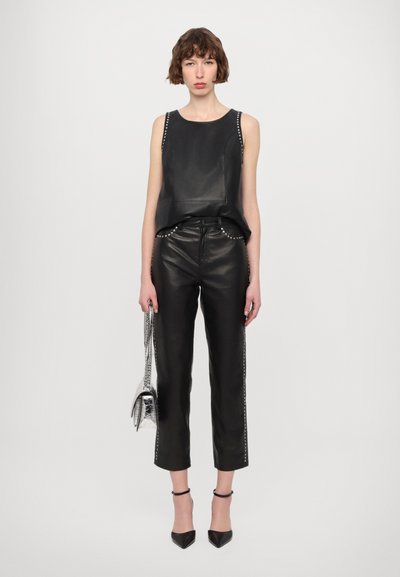 Black leather sleeveless top with studded accents, paired with black leather trousers featuring studded side details. Model holds a metallic bag.